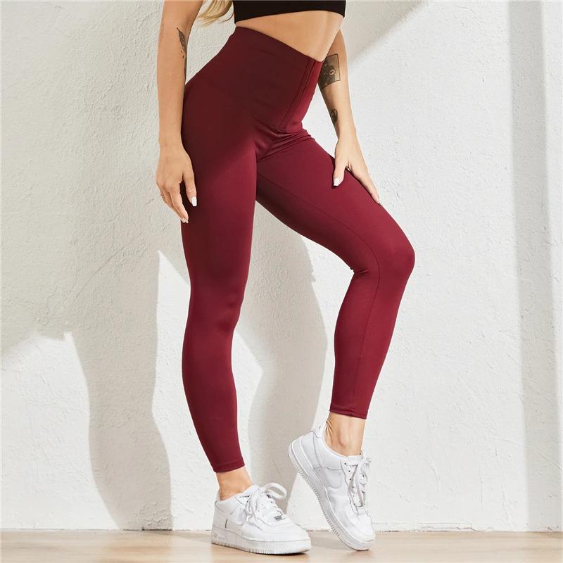 Frau in bordeauxroter Shaping-Leggings, hoher Bund, sportlich, figurformend, weiße Sneaker.
