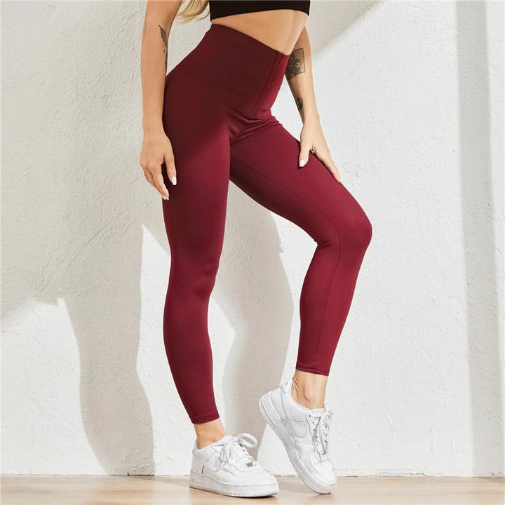 Frau in bordeauxroter Shaping-Leggings, hoher Bund, sportlich, figurformend, weiße Sneaker.