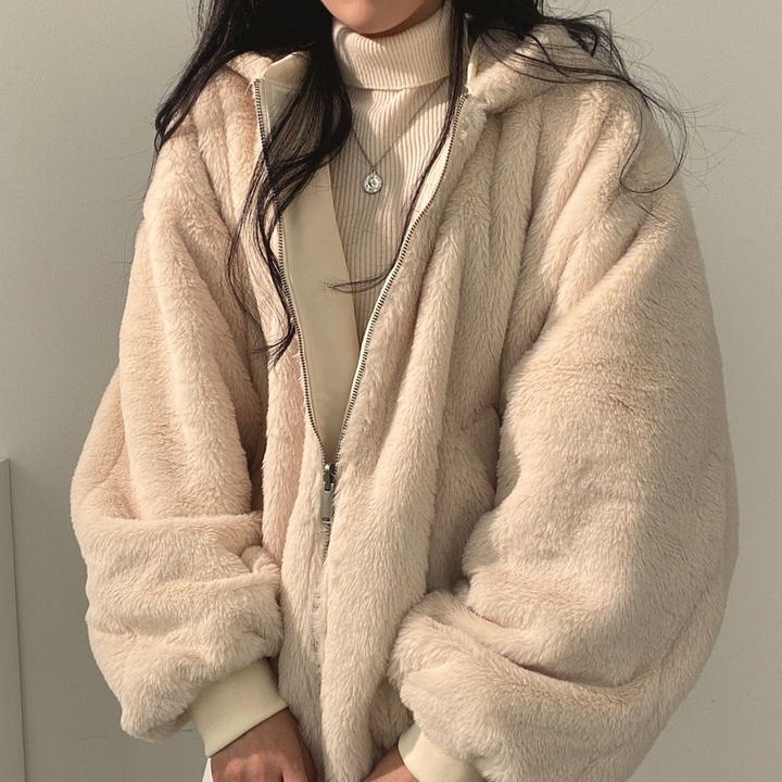 Frau in beiger Plüschjacke mit Kapuze, Reißverschluss, Rollkragenpullover, Wintermode.