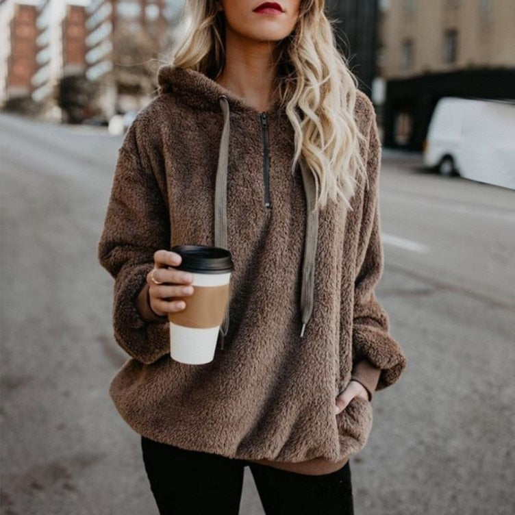 Frau in braunem Fleece-Hoodie mit Kaffeebecher, lässige Straßenmode, Herbstbekleidung.