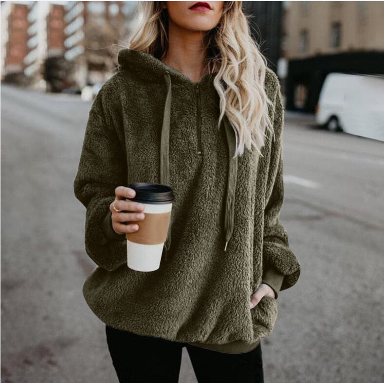 Frau in olivgrünem Fleece-Hoodie hält Kaffeebecher, lässige Straßenmode, Herbstoutfit.