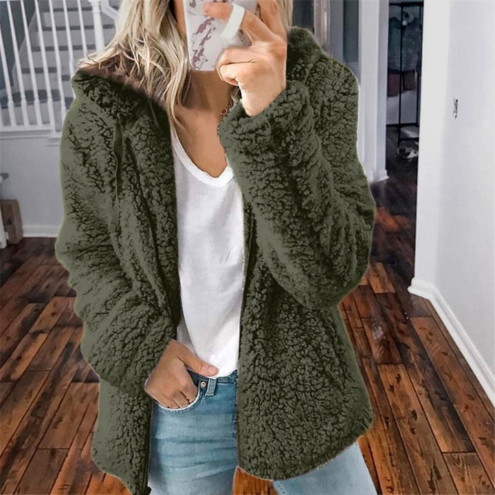 Frau in grüner Teddyfelljacke, weißem T-Shirt und Jeans in modernem Innenraum.