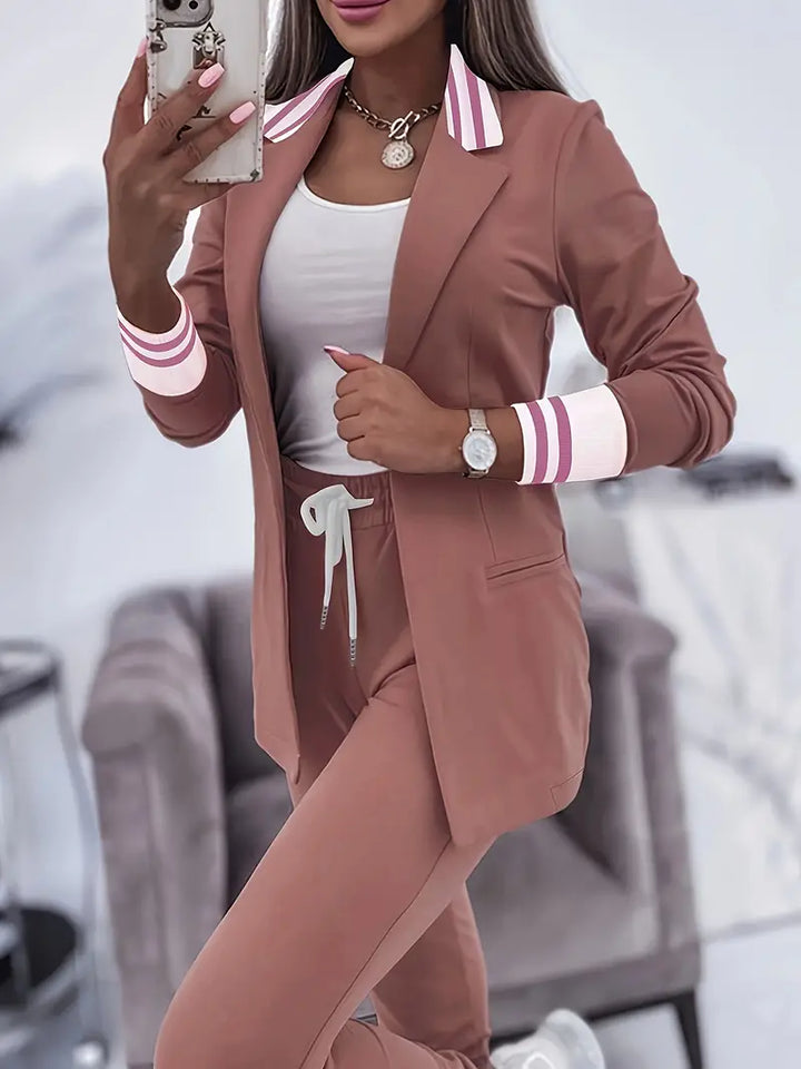 Frau in braunem Anzug mit rosa Details, weißem Top, Smartphone, Armbanduhr, Kette.