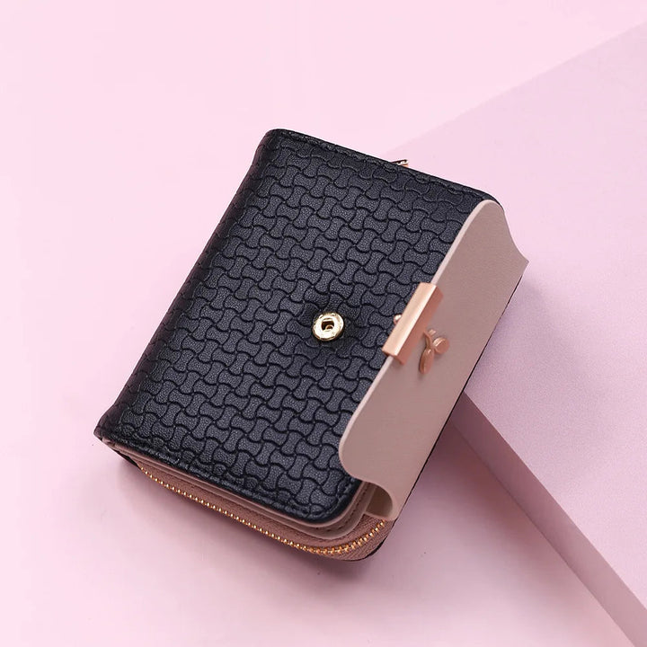 Schwarze Damen-Geldbörse aus Leder mit goldenen Akzenten auf rosa Hintergrund.