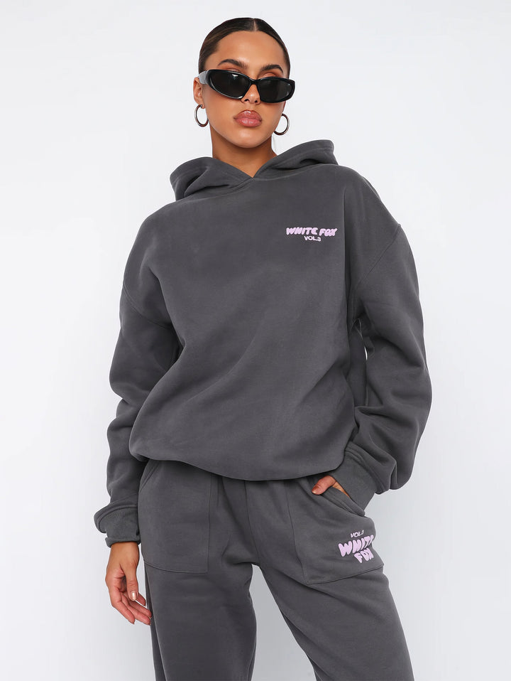 Frau in grauem Hoodie und Jogginghose, Sonnenbrille, lässige Mode, Streetwear-Look.