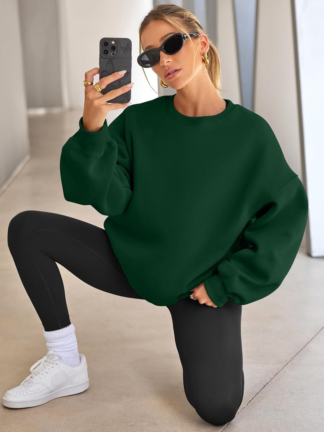Frau in grünem Oversize-Pullover, schwarze Leggings, Sonnenbrille, macht Selfie, modisch.