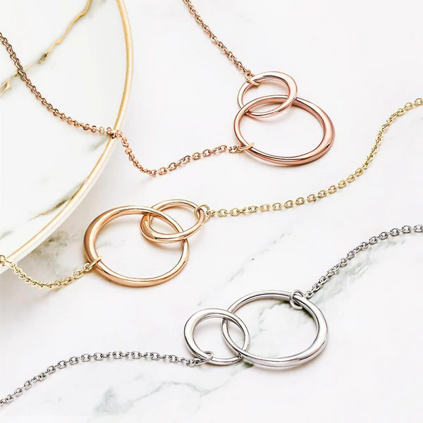 Drei ineinandergreifende Halsketten in Gold, Silber und Roségold auf Marmorhintergrund.