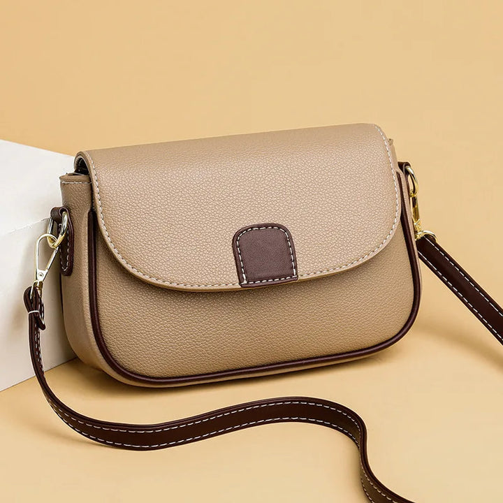 Beige Umhängetasche aus Leder mit braunen Akzenten und verstellbarem Riemen, modisch und elegant.