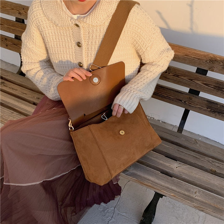 Frau mit brauner Umhängetasche aus Leder auf Holzbank, Herbstmode, Strickjacke, Plisseerock.