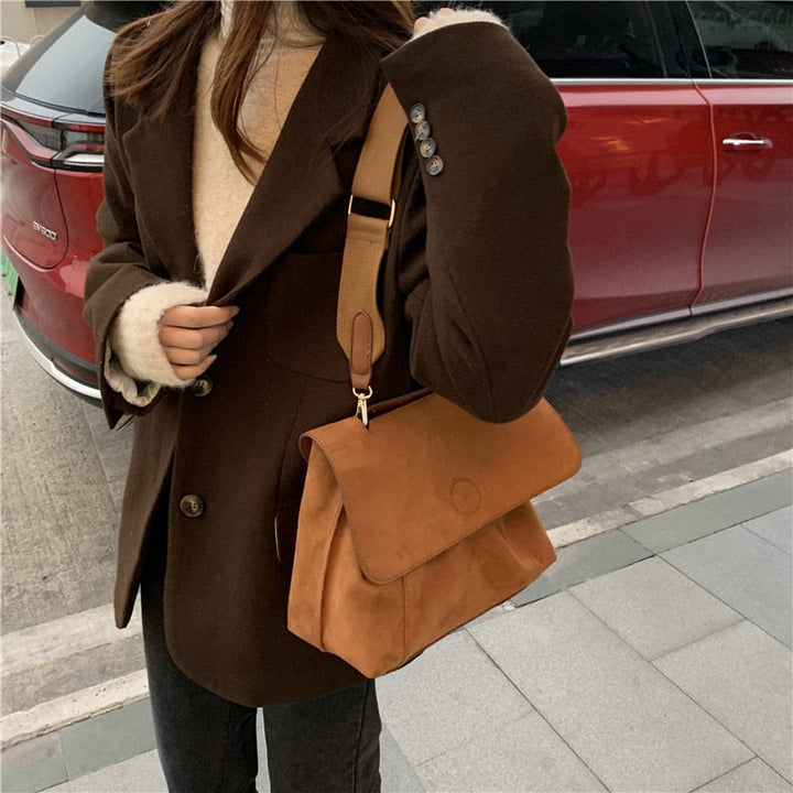 Frau mit brauner Wildledertasche, eleganter Mantel, rotes Auto im Hintergrund.