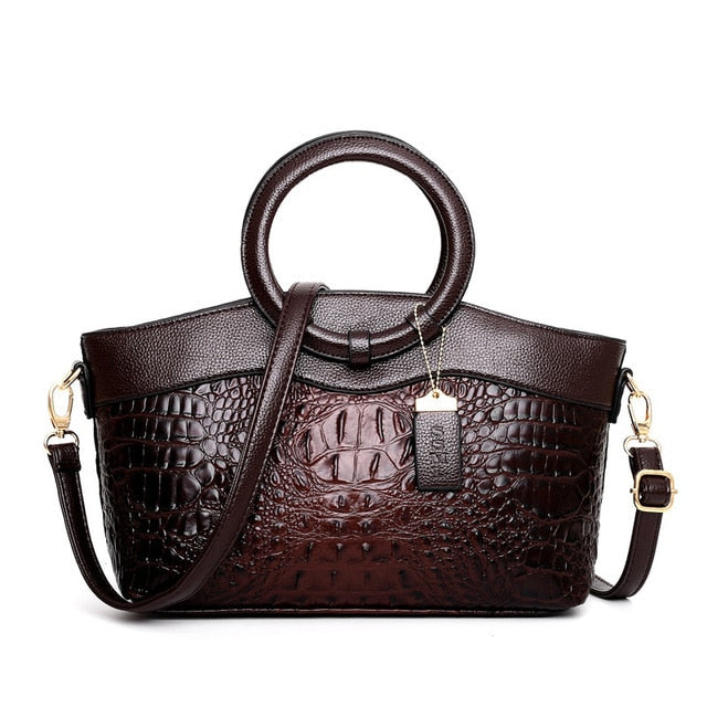 Damenhandtasche aus braunem Leder mit Krokodilprägung, runder Griff, verstellbarer Schulterriemen.