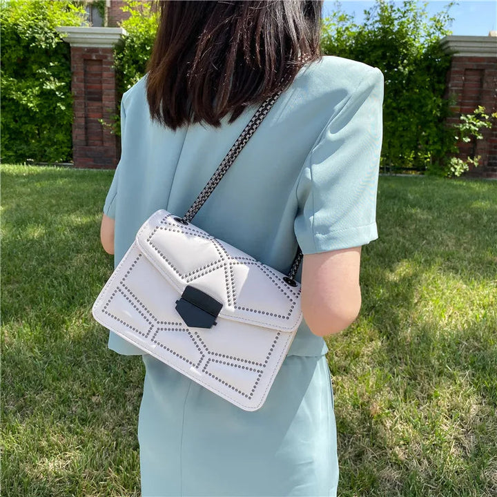 Frau mit weißer Lederhandtasche, Kettengurt, geometrisches Muster, im Freien.