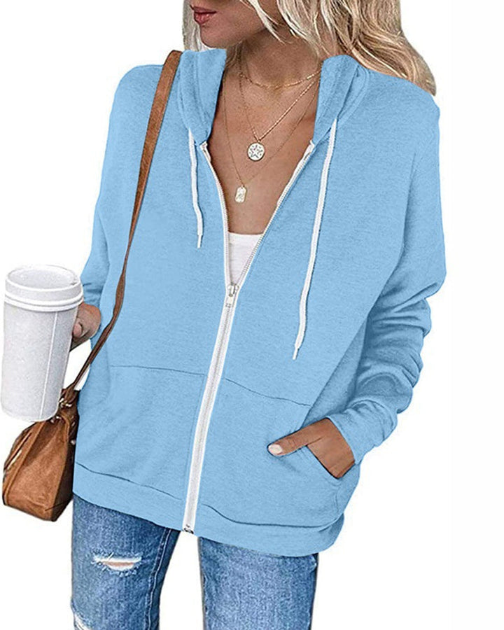 Frau in hellblauer Kapuzenjacke mit Reißverschluss, Kaffeebecher, braune Tasche, lässiger Stil.