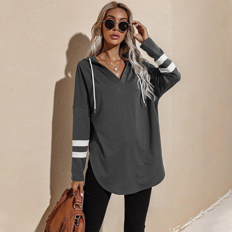 Frau in grauem Hoodie mit Streifen, Sonnenbrille, braune Tasche, lässige Mode.