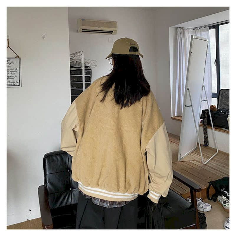 Person in beiger Oversize-Jacke und Cap in modernem Wohnzimmer mit Spiegel und Ledersessel.
