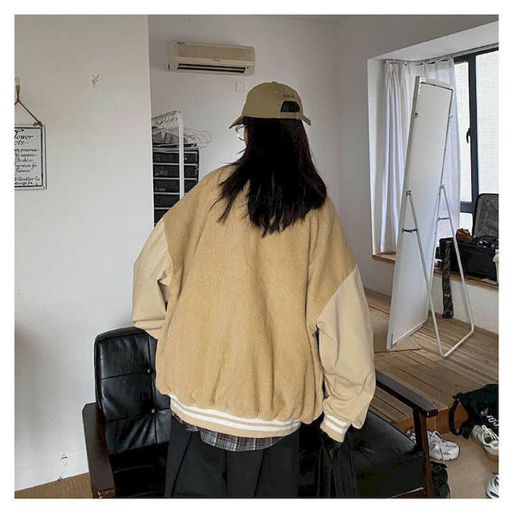 Person in beiger Oversize-Jacke und Cap in modernem Wohnzimmer mit Spiegel und Ledersessel.