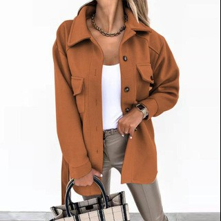 Frau in brauner Jacke, weißem Top, beigen Hosen, hält karierte Handtasche, modisch, elegant.