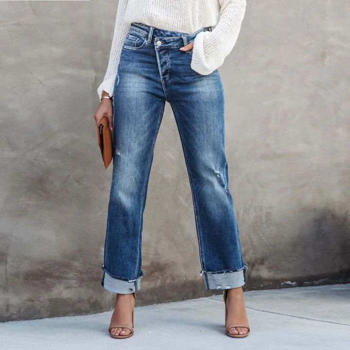 Frau in blauer Jeans und weißem Pullover, hält braune Clutch, trägt Sandalen.