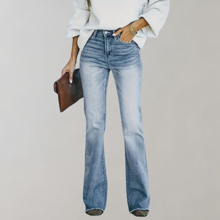 Frau in blauer Schlagjeans und weißem Pullover, hält braune Clutch.