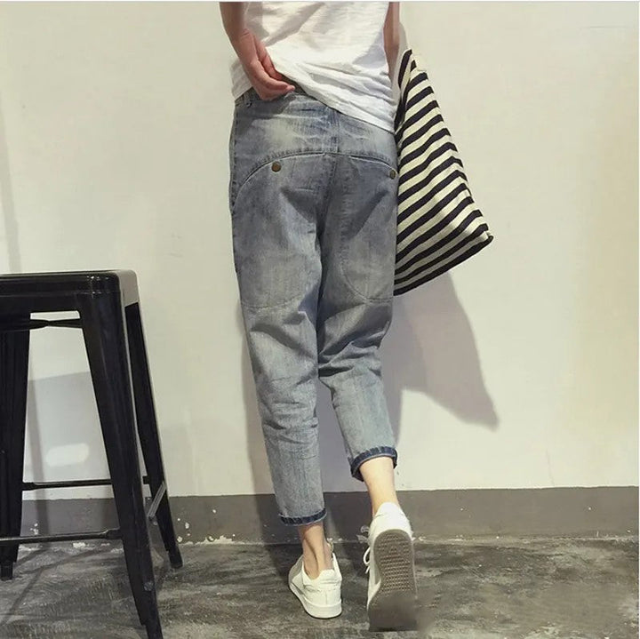 Person in blauer Jeans und weißen Sneakers, gestreifte Tasche, lässiger Stil, Rückansicht.