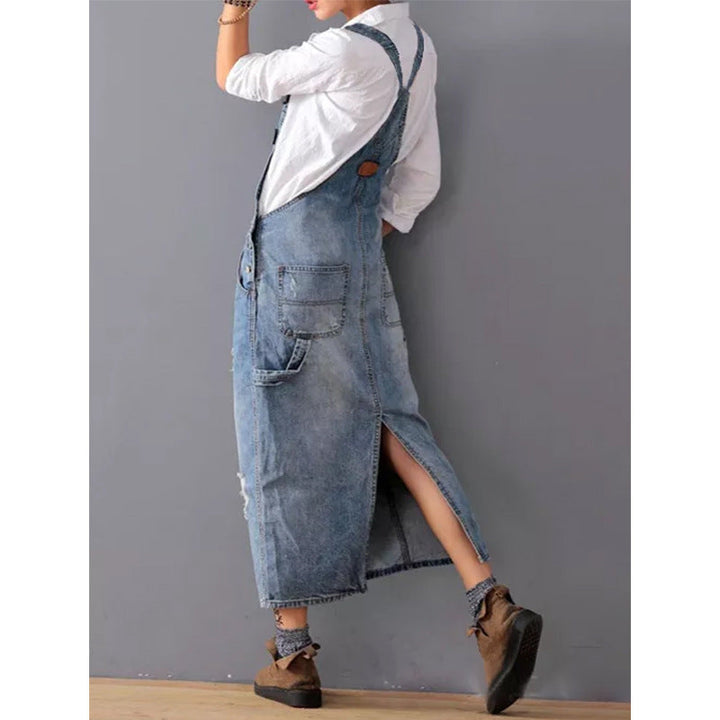 Frau in langem, blauem Jeanskleid mit Taschen, weißem Hemd und braunen Schuhen.