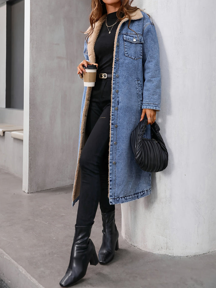 Frau in blauem Jeansmantel mit schwarzer Tasche und Stiefeln, hält Kaffeebecher.