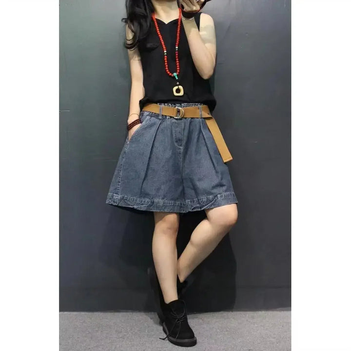 Frau in schwarzem Top und Jeansrock, rotes Halsband, brauner Gürtel, schwarze Stiefel.