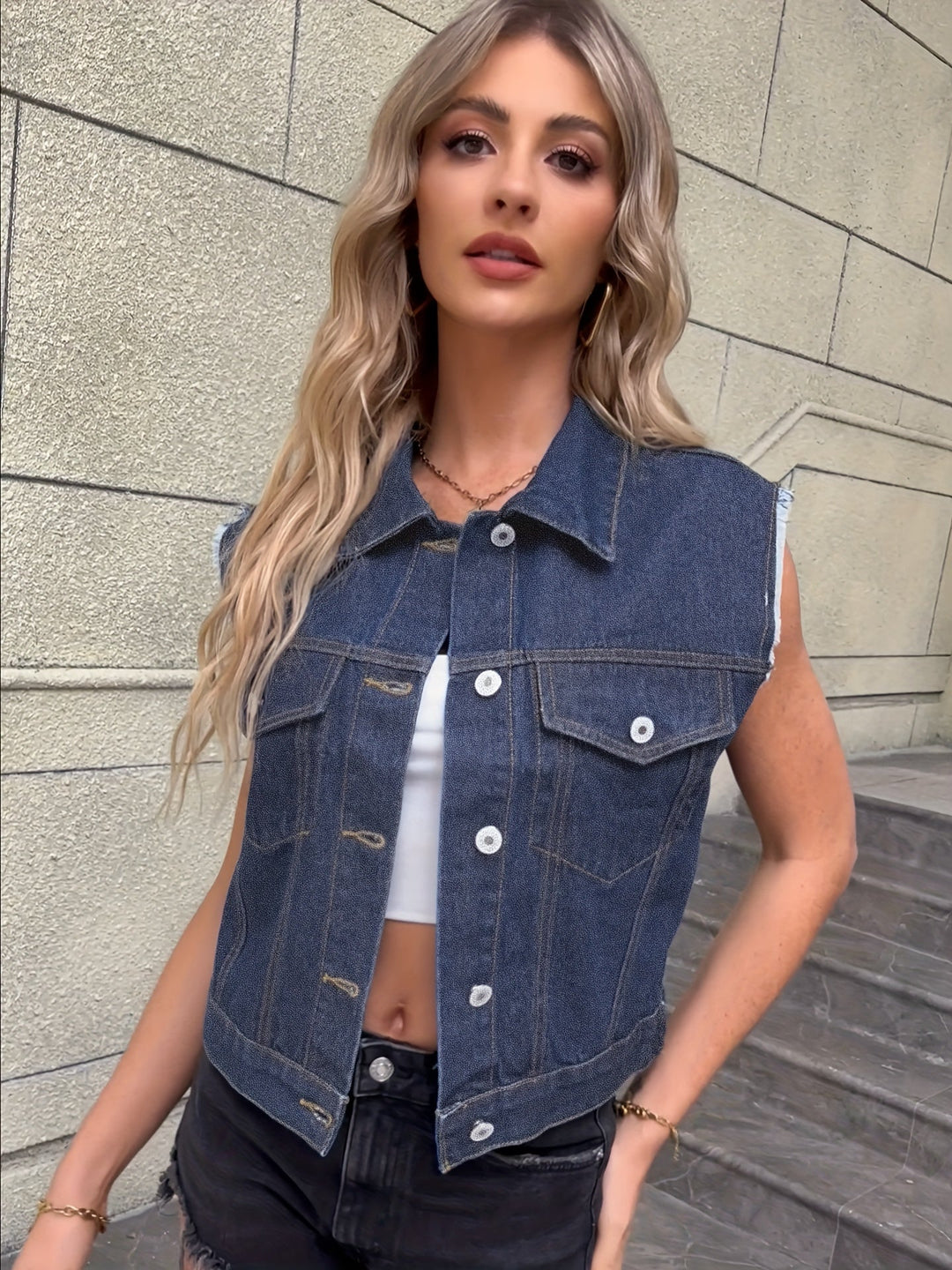 Frau in ärmelloser Jeansweste, weißem Top, schwarze Jeans, modisch, urbaner Stil.