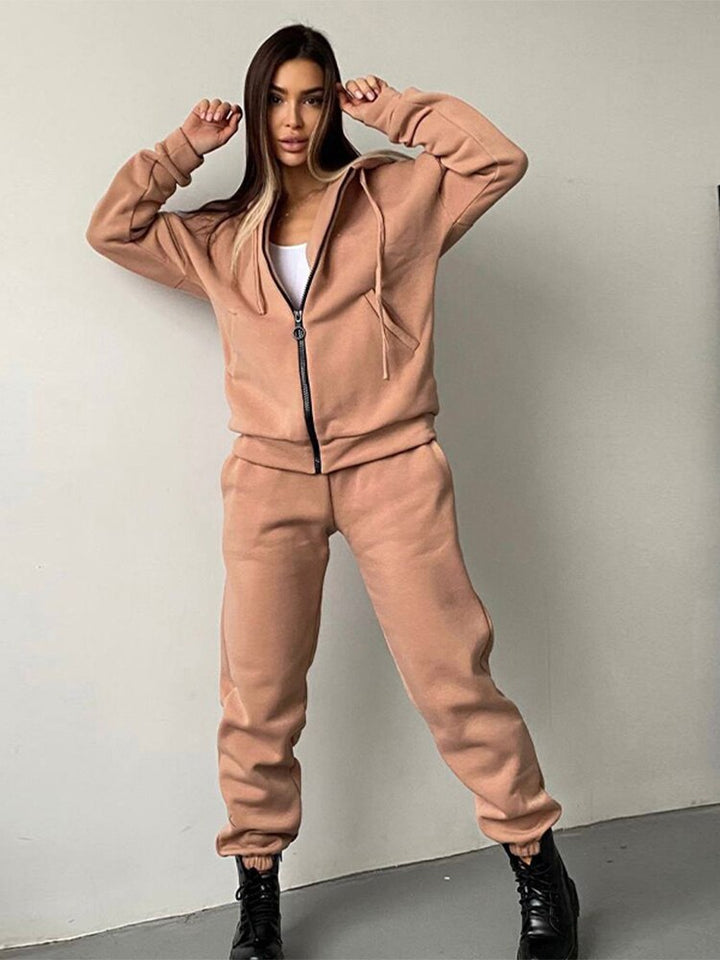 Frau in beigem Jogginganzug, Kapuzenjacke, Jogginghose, schwarze Stiefel, Freizeitmode.
