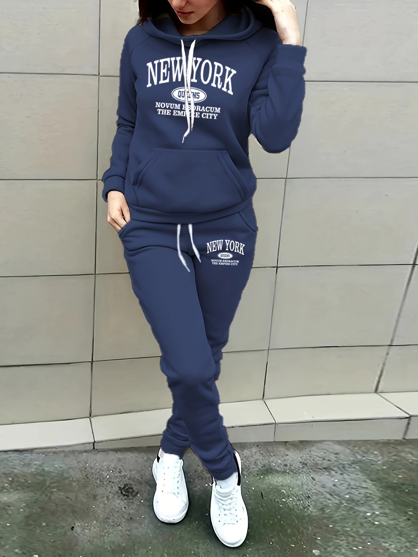 Frau in dunkelblauem New York Hoodie und Jogginghose, weiße Sneakers, lässige Mode.