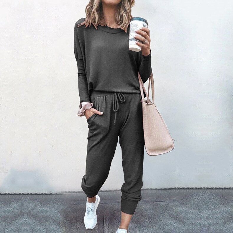 Frau in grauem Jogginganzug mit Kaffeebecher und beiger Tasche, lässige Mode.