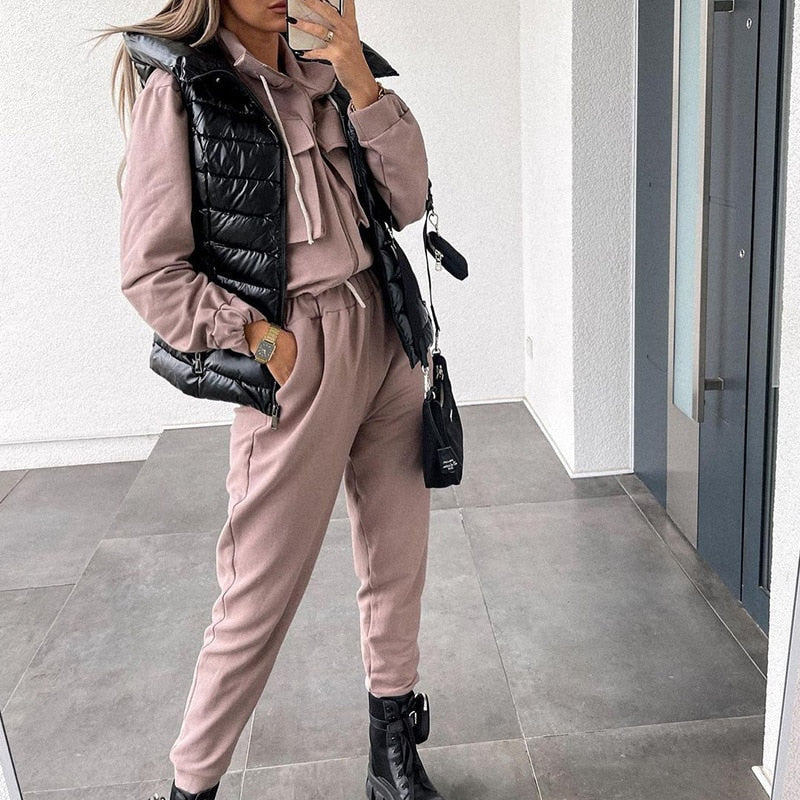 Frau in rosa Jogginganzug mit schwarzer Steppweste und Stiefeln, modisches Freizeitoutfit.