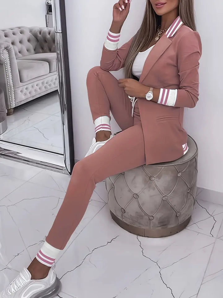 Frau in rosa Jogginganzug mit Sneakers, sitzt auf grauem Hocker, modernes Wohnzimmer.