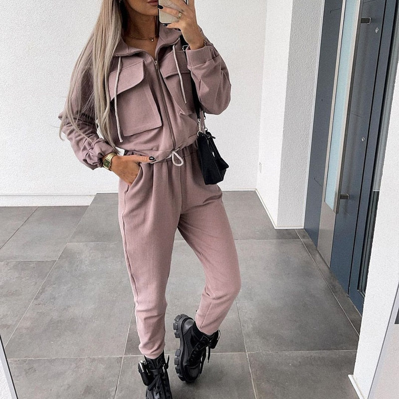 Frau in rosa Jogginganzug, schwarze Stiefel, schwarze Tasche, moderne Freizeitmode, Innenraum.