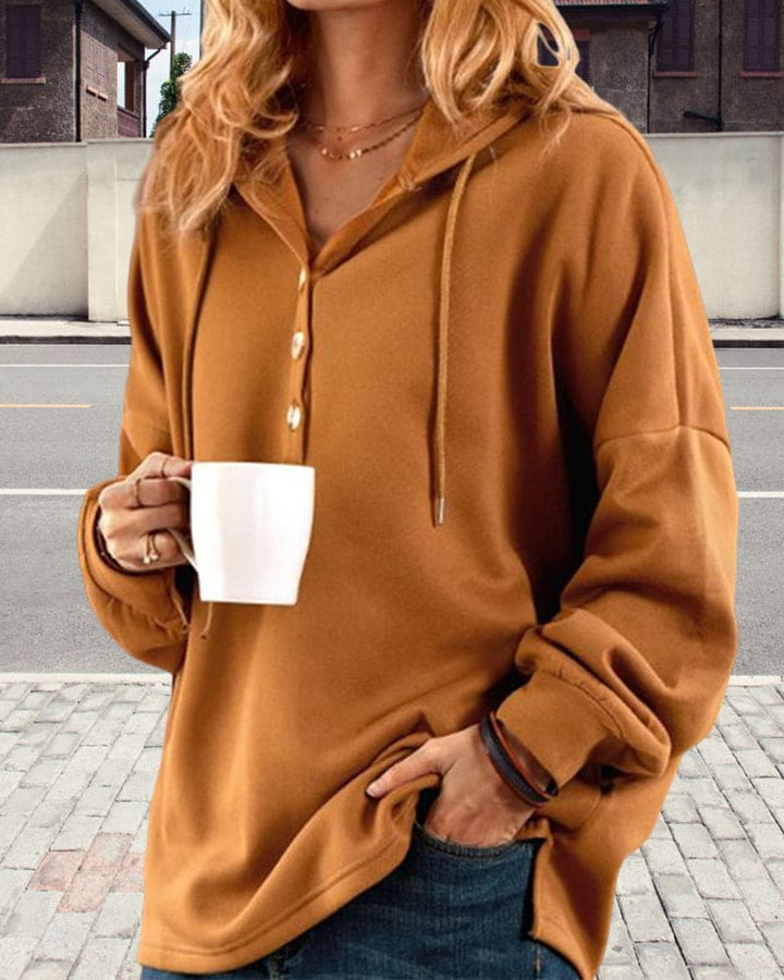 Frau in braunem Hoodie mit Kapuze hält weiße Tasse, lässige Herbstmode, Straßenhintergrund.
