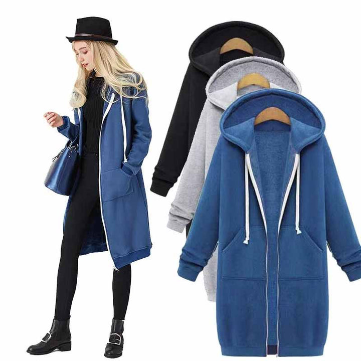 Frau in blauem Kapuzenmantel, schwarze Leggings, Hut, mit blauer Tasche, drei Mäntel im Hintergrund.