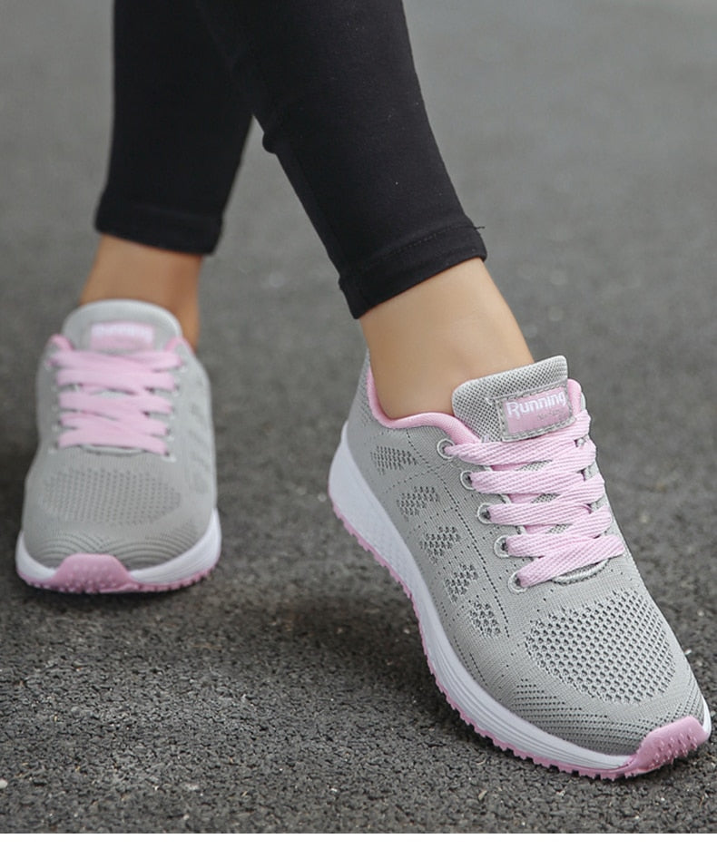 Graue Damen-Laufschuhe mit rosa Akzenten, atmungsaktiv, auf Asphalt getragen.
