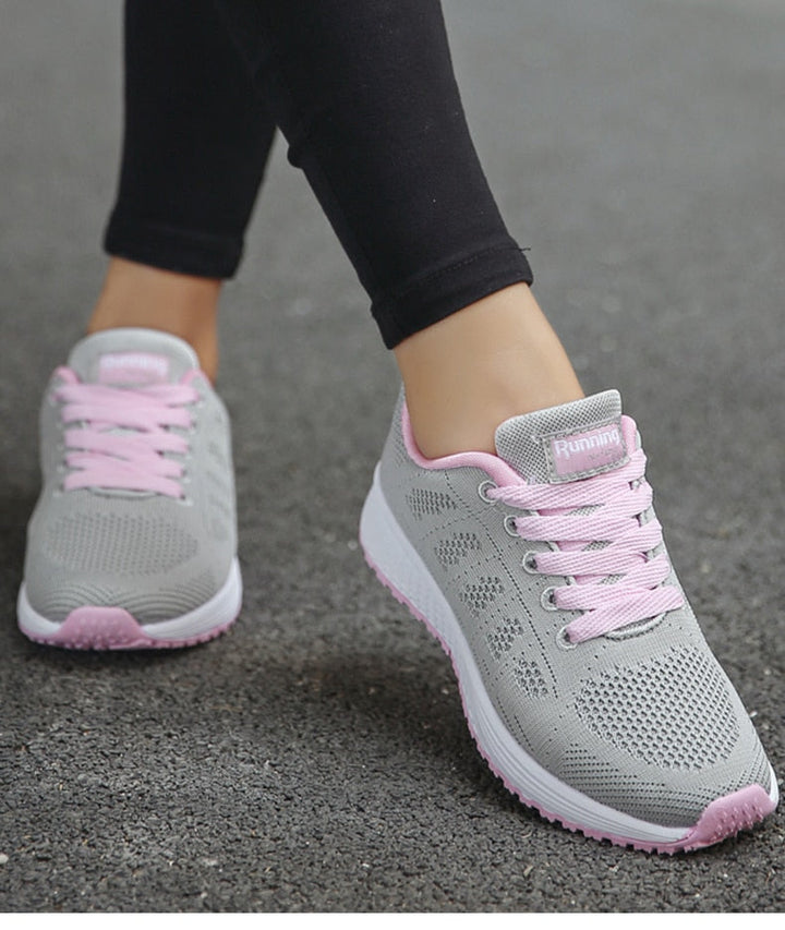 Graue Damen-Laufschuhe mit rosa Akzenten, atmungsaktiv, auf Asphalt getragen.