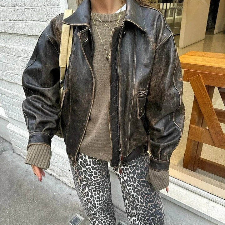 Frau in brauner Lederjacke, grauem Pullover und Leopardenhose auf der Straße.