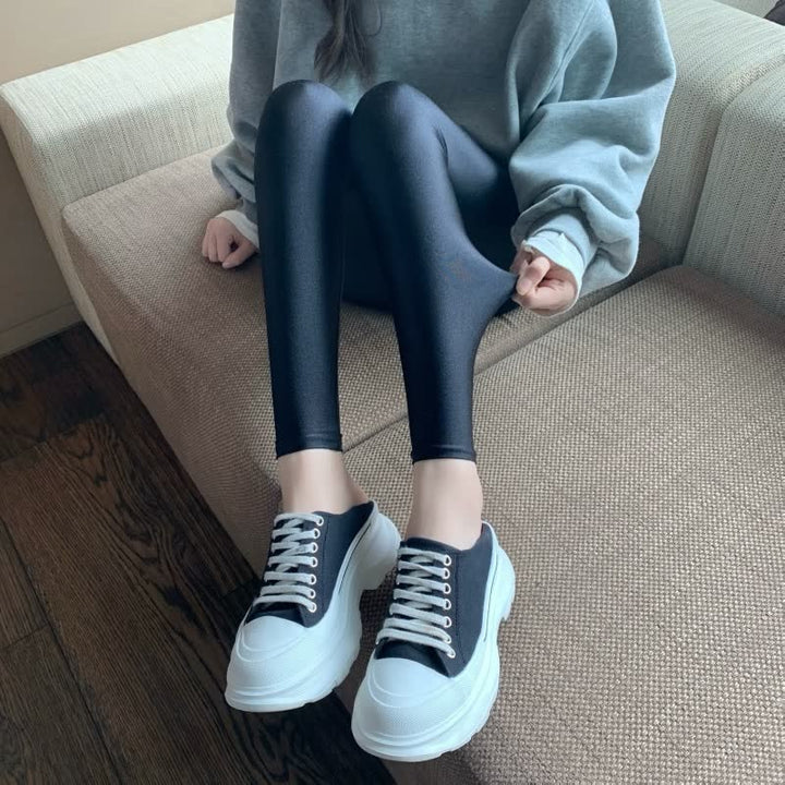 Frau trägt schwarze Leggings und weiße Sneaker auf Sofa, gemütliche Mode, Freizeitkleidung.