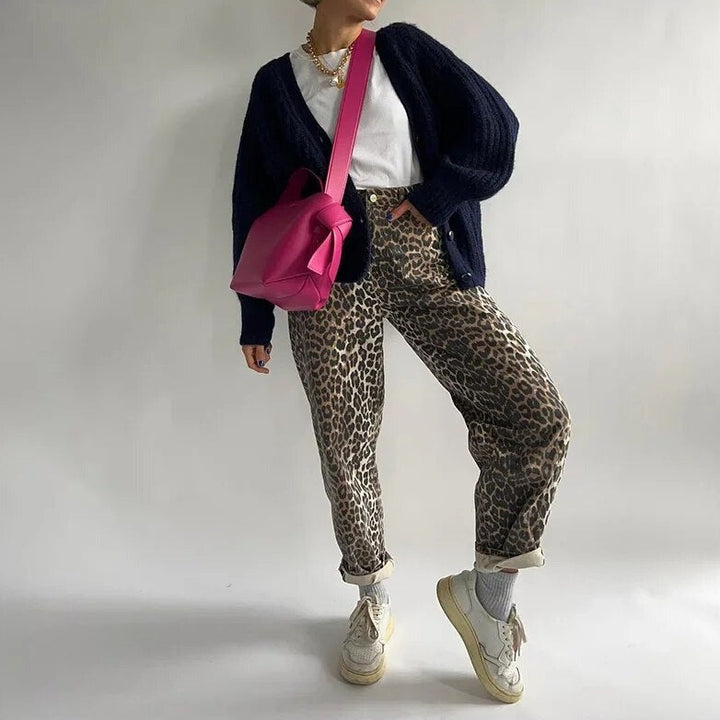 Frau in Leopardenhose, weißem T-Shirt, schwarzer Strickjacke, pinker Tasche, weißen Sneakers.