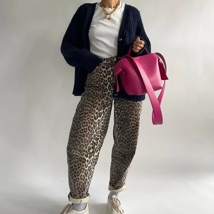 Frau mit Leopardenhose, schwarzer Strickjacke, weißem T-Shirt und pinker Handtasche.