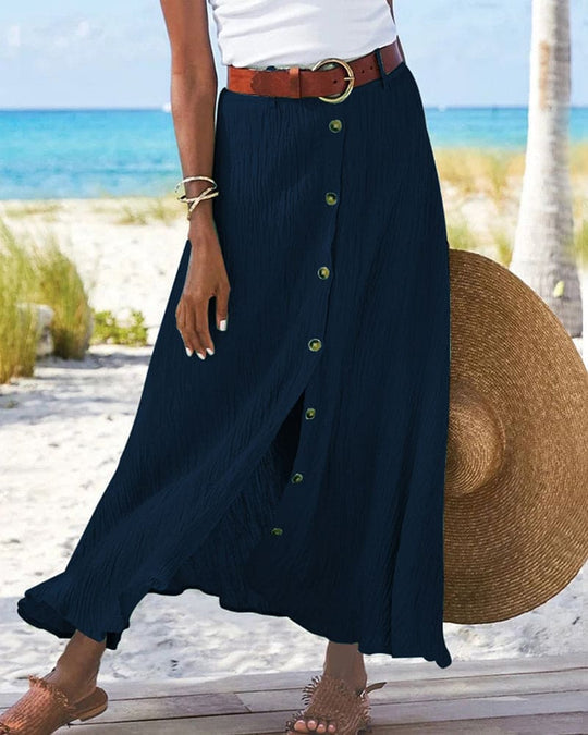 Frau am Strand mit dunkelblauem Maxirock, weißem Top, Strohhut und braunem Gürtel.