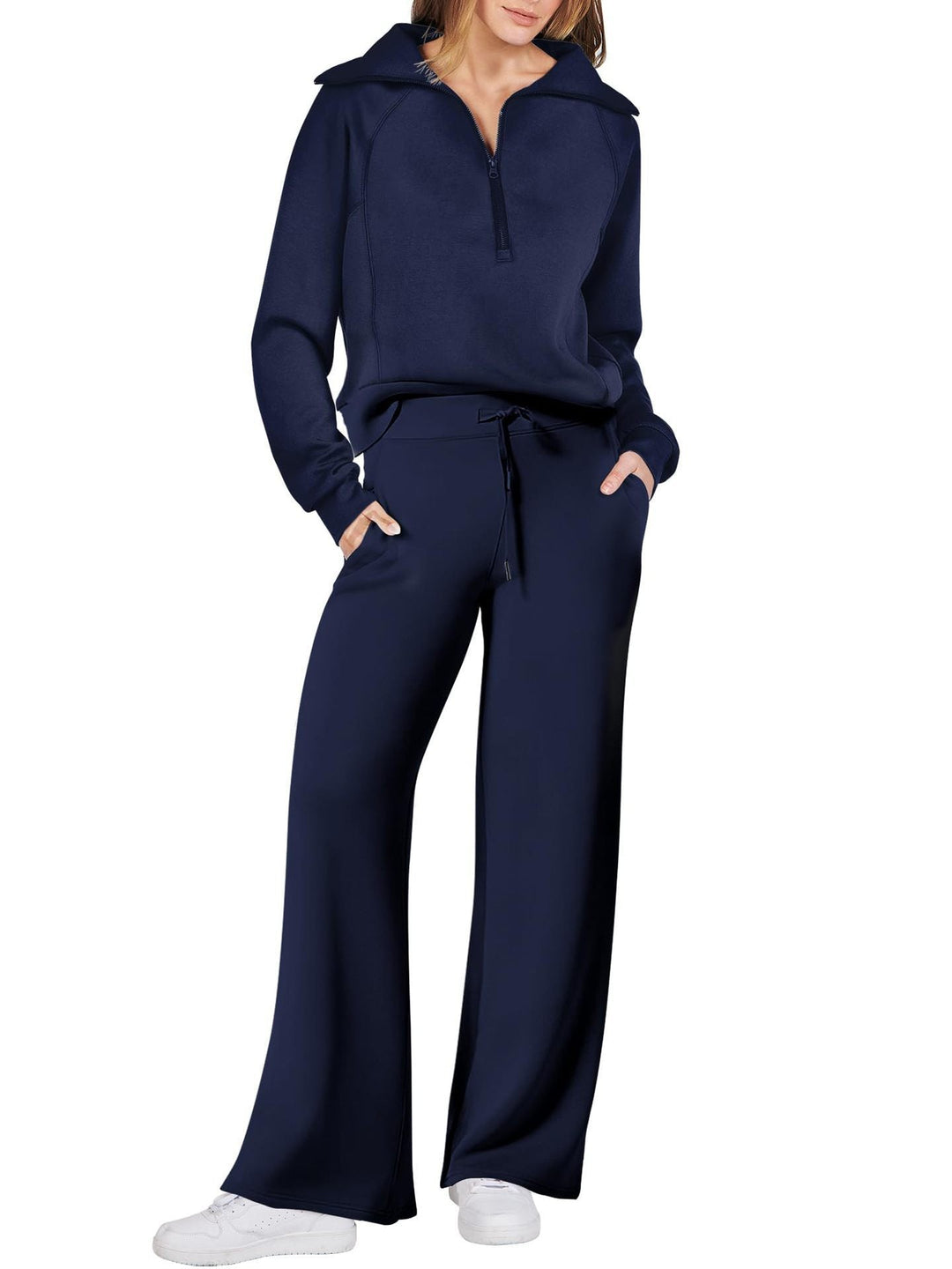 Frau in dunkelblauem Jogginganzug, Reißverschluss, weite Hose, weiße Sneaker, Freizeitmode.