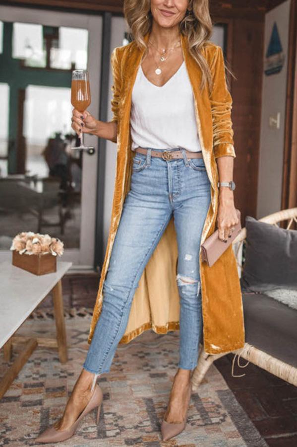 Frau in gelbem Samtmantel, weißem Top, blauer Jeans, hält Getränk, modisch, elegant, modern.