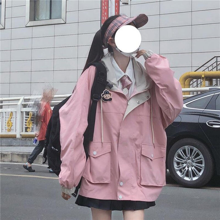 Frau in rosa Oversize-Jacke mit Kapuze und Rucksack auf Straße vor Gebäude.