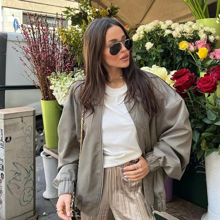 Frau in übergroßer, grauer Herbstjacke vor Blumenladen, trägt Sonnenbrille und weiße Bluse.