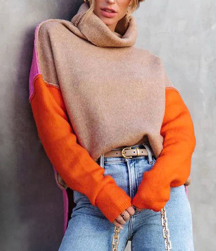 Frau in beigem Rollkragenpullover mit orangefarbenen Ärmeln und blauer Jeans.