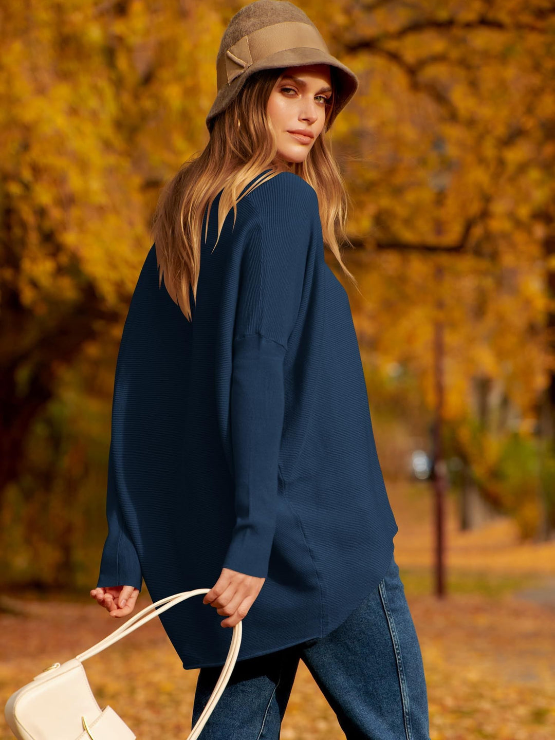 Frau im blauen Pullover und Hut im Herbstpark, modische Herbstkleidung, Freizeitlook.