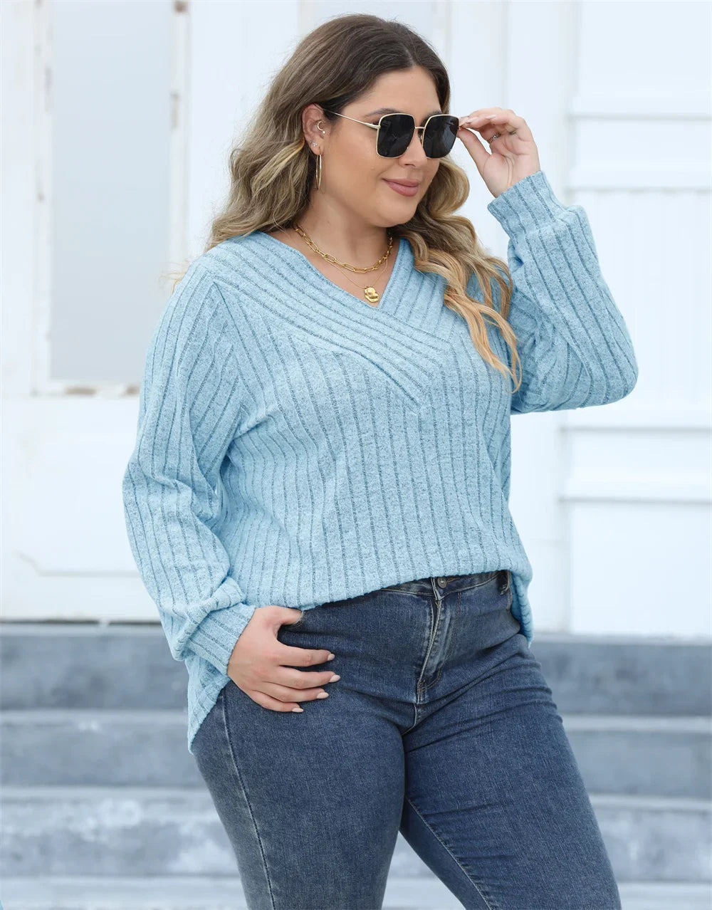Frau in hellblauem Strickpullover und Jeans, trägt Sonnenbrille, lässige Mode.